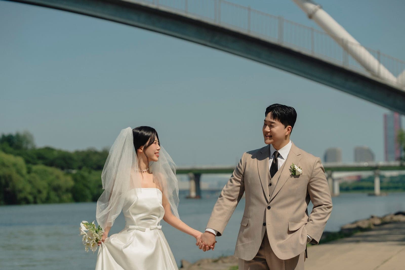 다리를 배경으로 손을 맞잡은 신랑과 신부